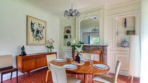 A dining area with a round wooden table set for four, surrounded by white upholstered chairs. - Le Logis - Charmante Maison Proche Plage (Téteghem-Coudekerque-Village)