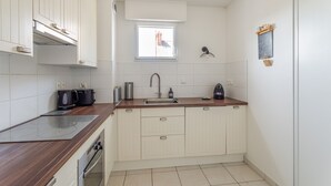 A compact kitchen with white cabinets, a wooden countertop, a built-in oven, a sink, and a window with a view of a building outside. - L'appart du Val - 100 m de la plage (Pléneuf-Val-André)