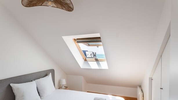A bedroom with a skylight, a bed, a bedside table, and a view of the sea through the skylight. - L'appart du Val - 100 m de la plage (Pléneuf-Val-André)