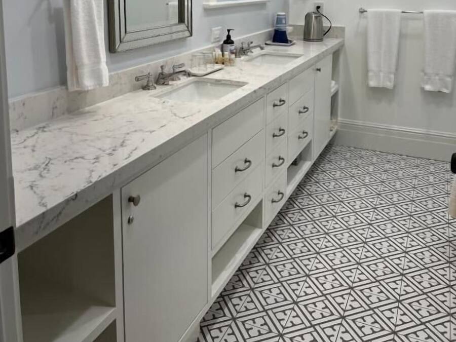 A bathroom with a marble sink, white cabinets, a large mirror, and patterned floor tiles.