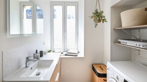 Een moderne badkamer met een grote spiegel, een wastafel, een raam en een wasmachine.