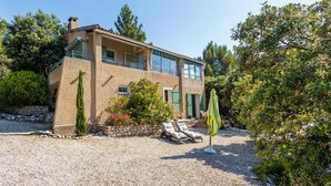 A two-story house with a balcony, a gravel driveway, and a garden with shrubs and a tree.