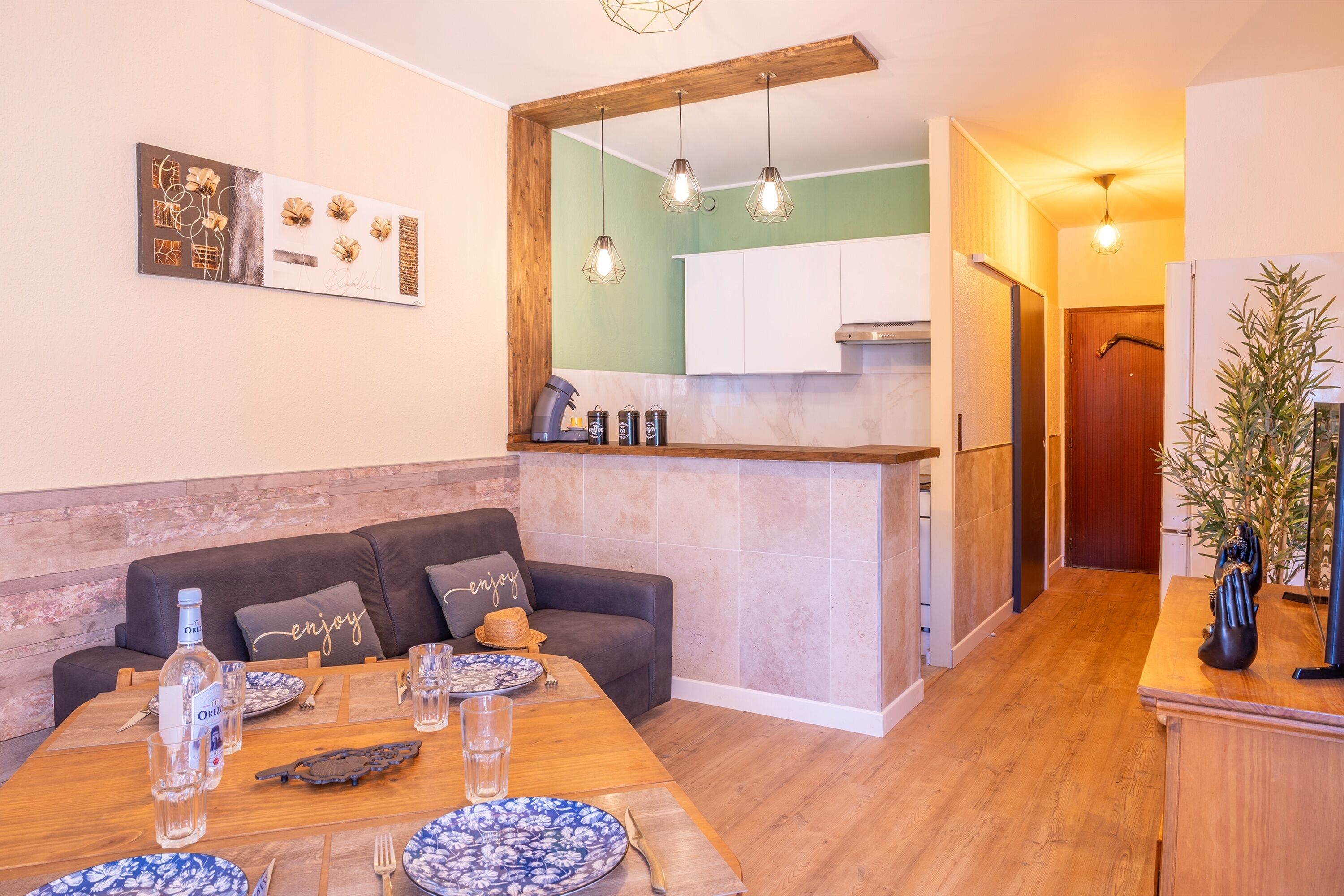 Een moderne woonkamer met een houten eettafel gedekt voor vier personen, een bank met kussens en een keuken op de achtergrond.