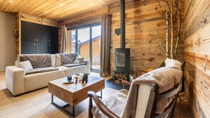 Un acogedor interior de cabaña con un sofá, una mesa de centro de madera, una silla, chimenea y un ventanal grande.