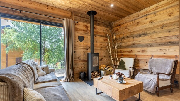 Un acogedor interior de cabaña con paredes y detalles de madera, un sofá, una silla, una mesa y una chimenea.