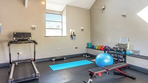 Un gimnasio con cinta de correr, pelotas de ejercicio, mancuernas y un banco.