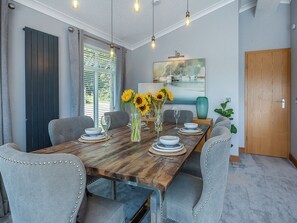 Un comedor con una mesa de madera, sillas tapizadas en gris y un florero con girasoles.