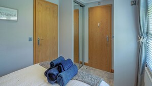 Habitación de hotel con cama, dos puertas de madera, un cuadro en la pared y una ventana con persianas.