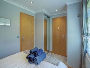 A hotel room with a bed, two wooden doors, a framed picture on the wall, and a window with blinds.