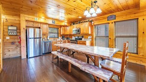 A wooden cabin interior with a kitchen, dining area, and a sign reading "Welcome to the Boulders."