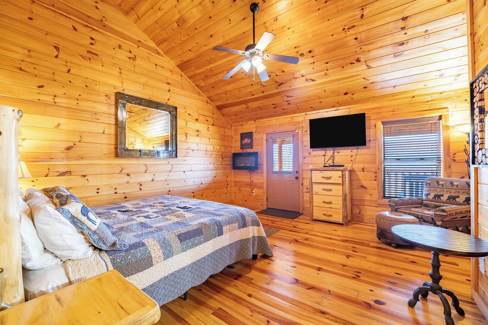 A cozy log cabin room with a bed, a dresser, a television, and a seating area.