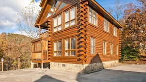 A log cabin with a stone foundation, multiple windows, and a balcony. - Center of Attention (Sevierville)