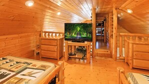 A cozy wooden cabin room with a television, a bed, and a small table. - Center of Attention (Sevierville)