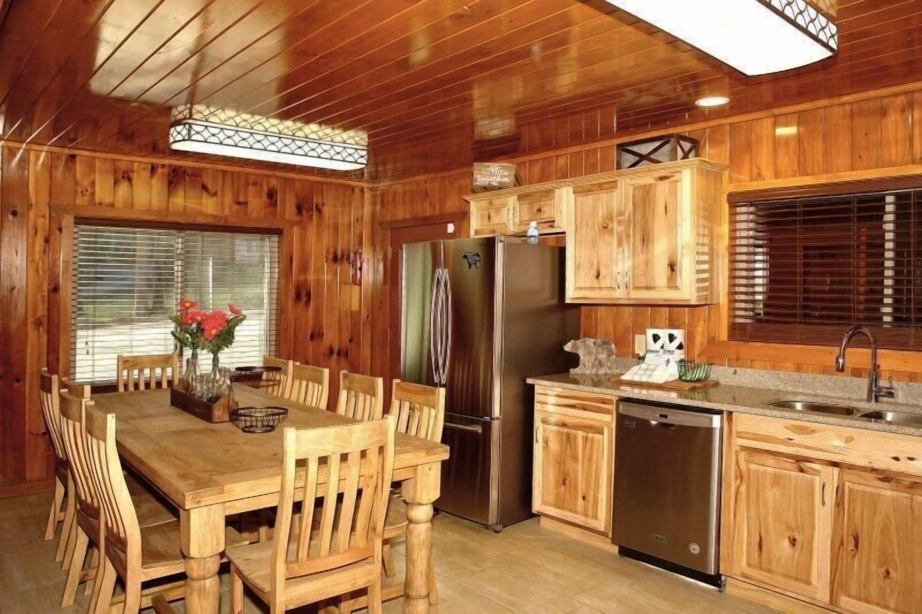 Une cuisine de style rustique, avec des éléments en bois, comprenant une table à manger, des chaises, un réfrigérateur, un lave-vaisselle et des placards en bois.