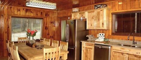 A wooden cabin-style kitchen with a dining table, chairs, a refrigerator, a dishwasher, and wooden cabinets.