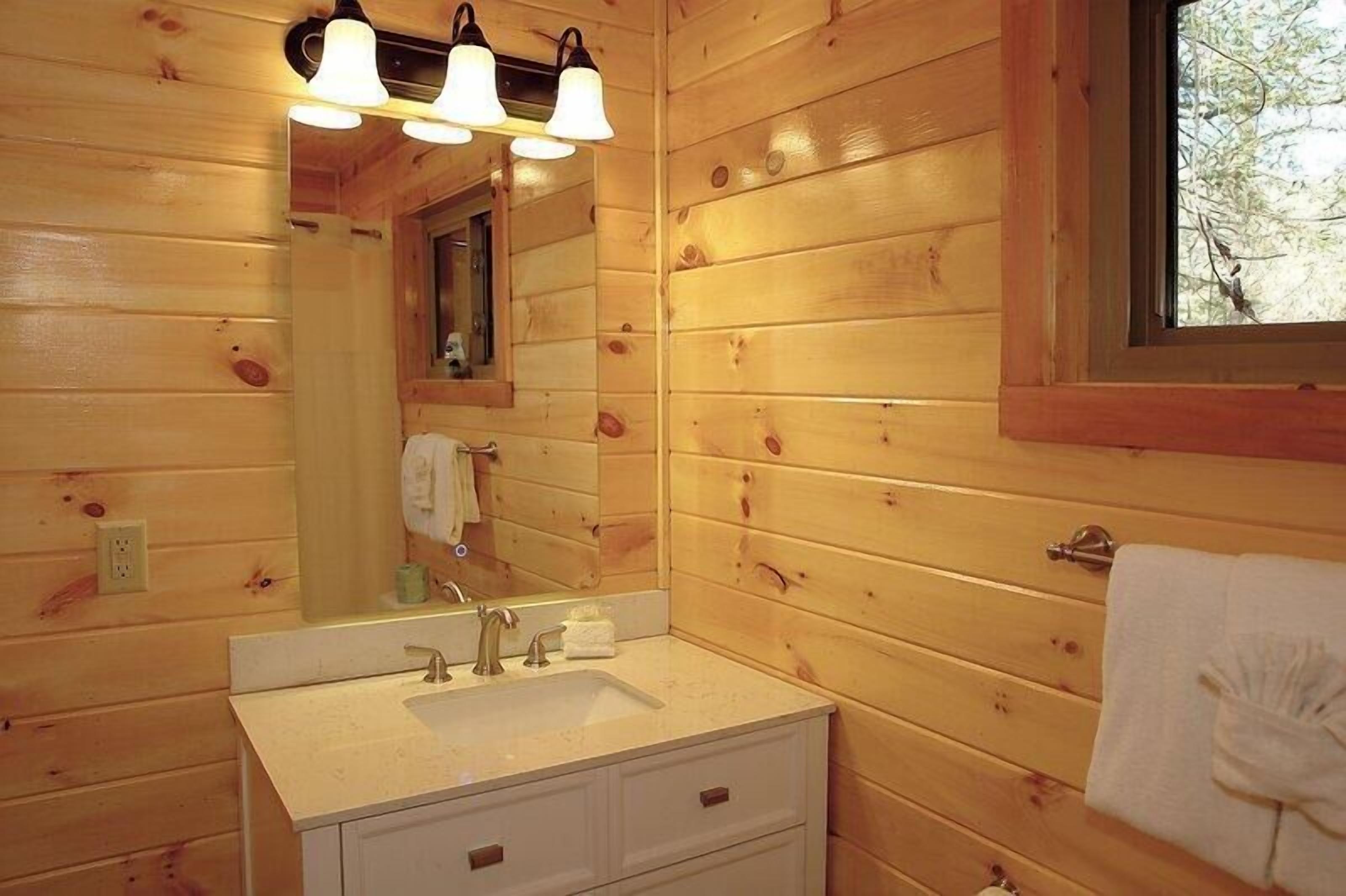 A wooden cabin bathroom with a sink, mirror, and two overhead lights.