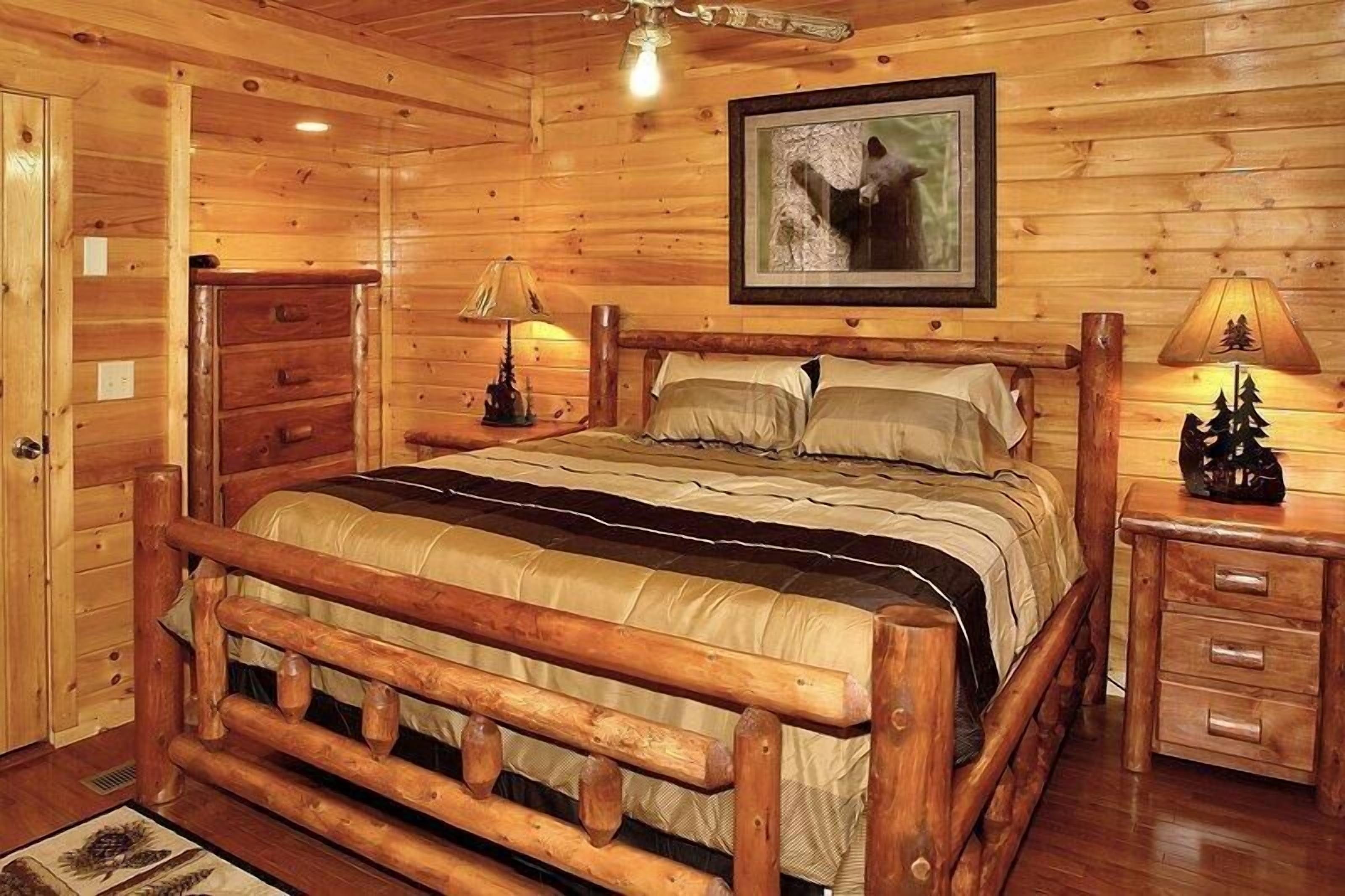 A wooden cabin bedroom with a bed, nightstands, a dresser, and a ceiling fan.