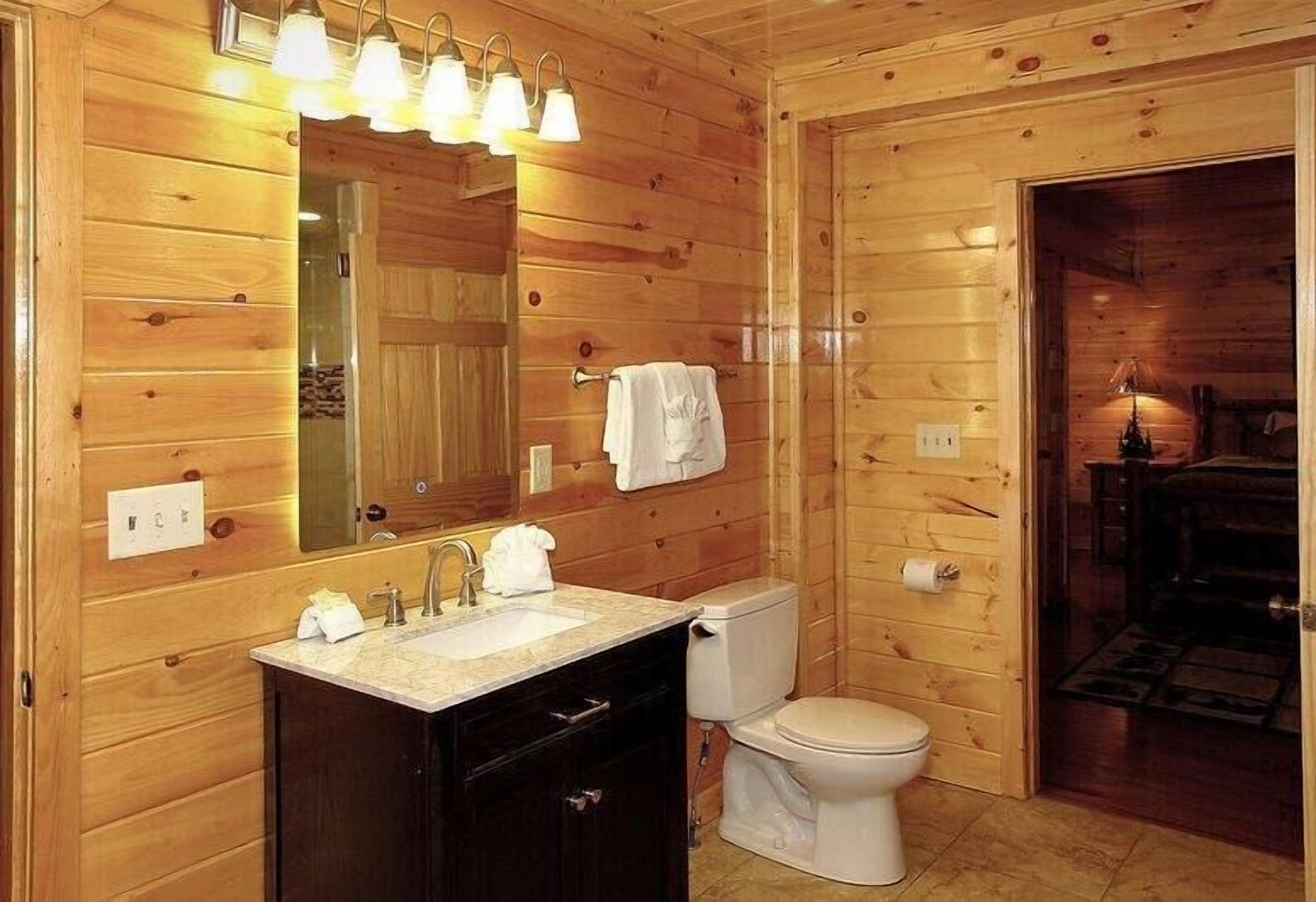 Baño de cabaña de madera con lavabo, espejo, inodoro y una toalla colgada en la pared.