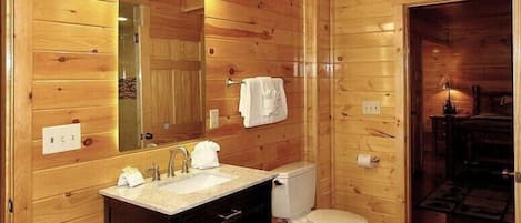 Baño de cabaña de madera con lavabo, espejo, inodoro y una toalla colgada en la pared.