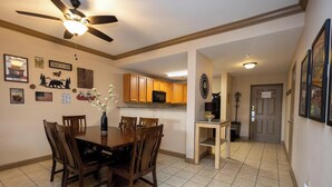A dining area with a wooden table and chairs, a ceiling fan, and a kitchen in the background. - Mountain View Condo 1501 (Pigeon Forge)