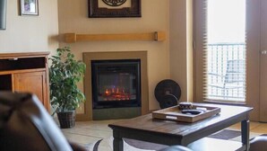 A living room with a fireplace, a ceiling fan, and a view of the outside through a door. - Mountain View Condo 1501 (Pigeon Forge)