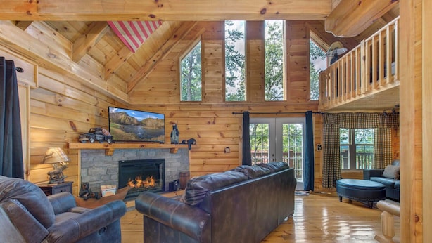 A log cabin interior with a stone fireplace, leather sofas, and a television mounted above it. - Beary Nice to Meet You! (Sevierville)