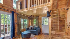 A cozy cabin interior with a wooden floor, a leather sofa, a round ottoman, a staircase, and a bear head decoration. - Beary Nice to Meet You! (Sevierville)
