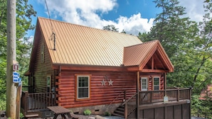A rustic log cabin with a metal roof, a wooden deck, and a stone wall. - Beary Nice to Meet You! (Sevierville)