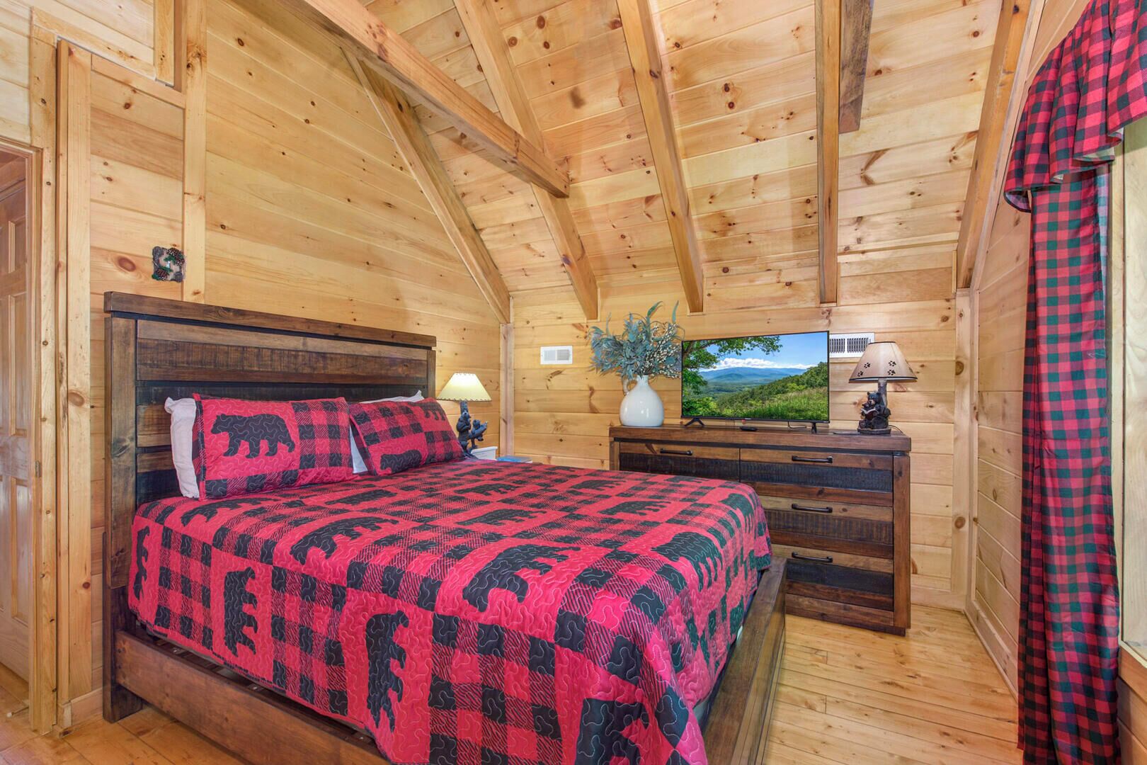 Habitación de cabaña de madera con cama, mesita de noche, televisor y ventana con vista al exterior.
