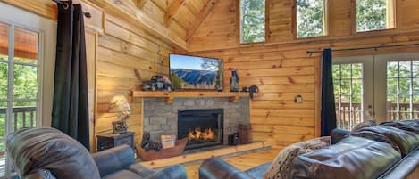 A cozy cabin interior with a stone fireplace, leather sofas, and a television.