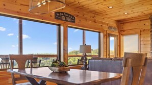 A wooden cabin interior with a dining table, chairs, a sofa, and a large window offering a scenic view. - Dolly Valley View (Sevierville)