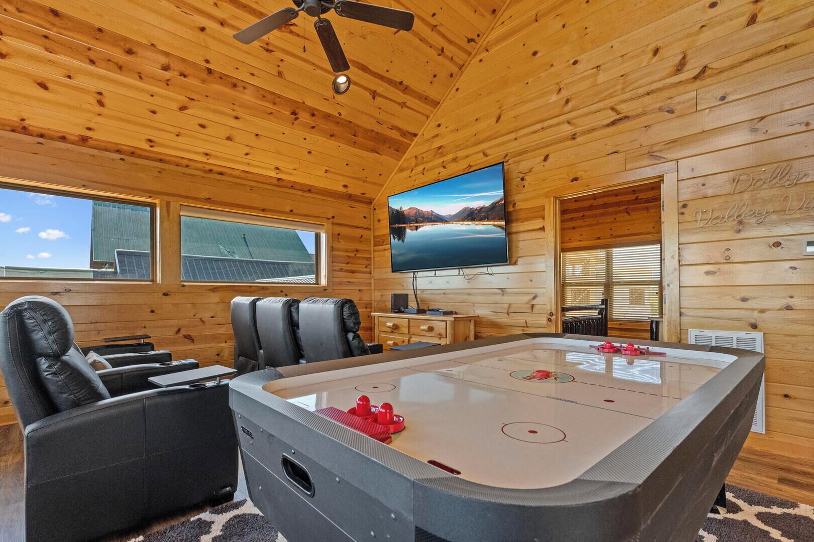 A wooden cabin interior with a large flat-screen TV, a pool table, and a ceiling fan.