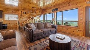 A cozy cabin interior with a wooden interior, a sofa, a coffee table, and a large window offering a view of the outdoors. - Dolly Valley View (Sevierville)