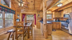 A wooden cabin interior with a dining area, kitchen, and large windows. - Catch Me If You Can (Pigeon Forge)