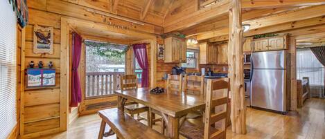 A wooden cabin interior with a dining table, benches, a kitchen area, and a ceiling fan.