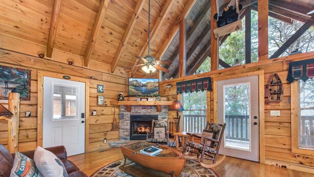 A cozy cabin interior with a fireplace, wooden walls, a rocking chair, and a large window. - Catch Me If You Can (Pigeon Forge)