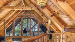 A wooden interior with a high ceiling, wooden beams, and a window with a view of trees. - Catch Me If You Can (Pigeon Forge)