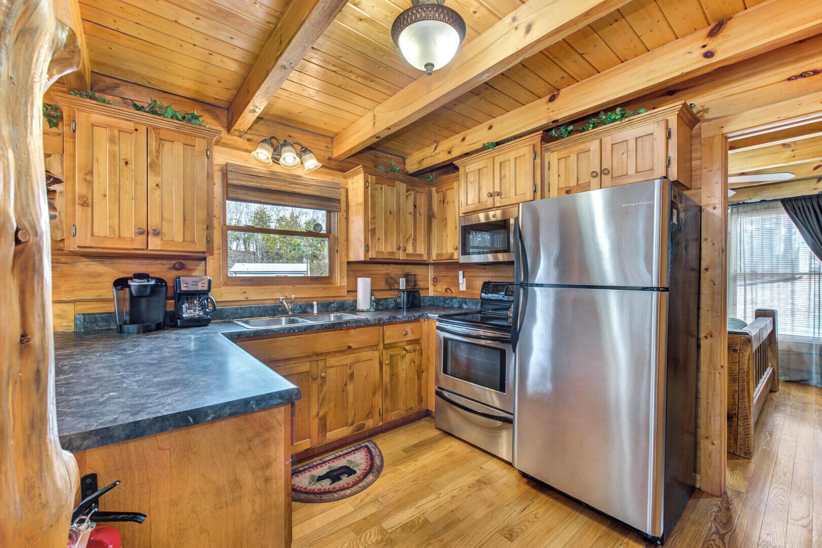 Une cuisine rustique, située dans une cabane en bois, équipée d’un réfrigérateur en acier inoxydable, d’une cuisinière, d’un four à micro-ondes et de meubles de rangement en bois.