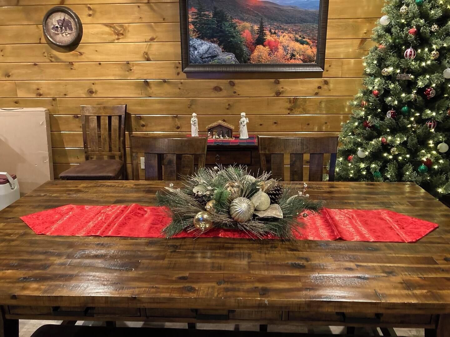 A wooden dining table with a red placemat, a Christmas tree, and a framed picture on the wall.