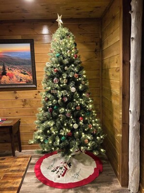 A Christmas tree with ornaments and lights, a framed picture on the wall, and a wooden floor. - Bear Paws Up (Pigeon Forge)