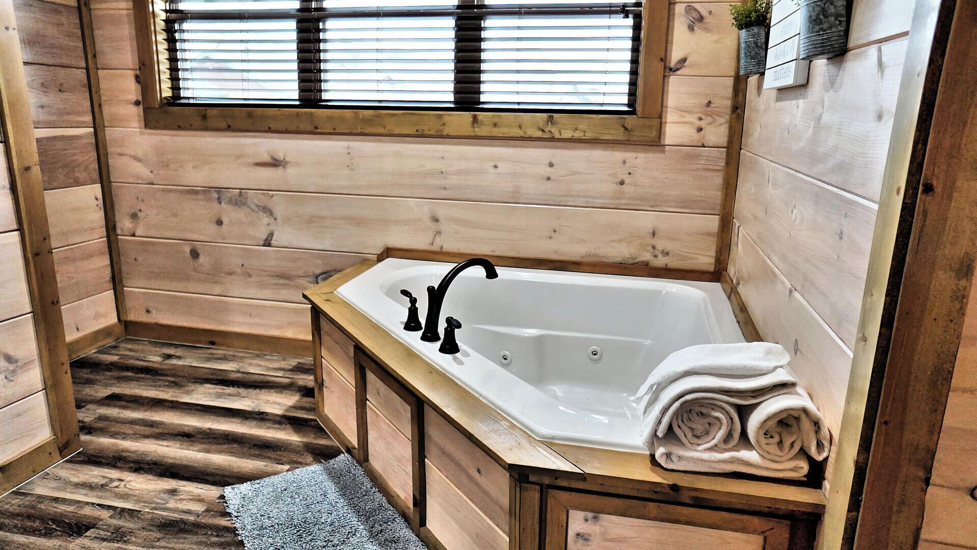 A wooden cabin bathroom with a bathtub, a window with blinds, and a towel rack.