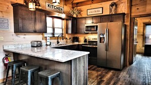 A kitchen with dark wood cabinets, stainless steel appliances, a marble countertop, and bar stools.