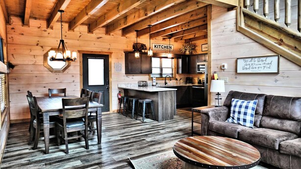 A cozy cabin interior with a wooden dining area, a kitchen, and a living space with a sofa and a coffee table.