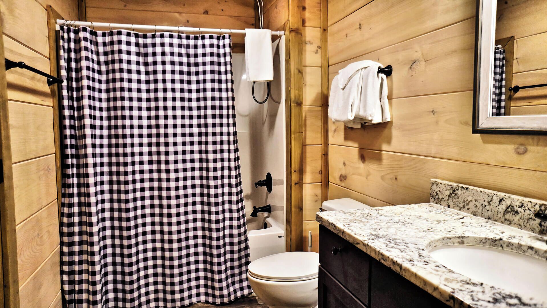 A bathroom with a checkered shower curtain, a toilet, and a sink with a granite countertop.