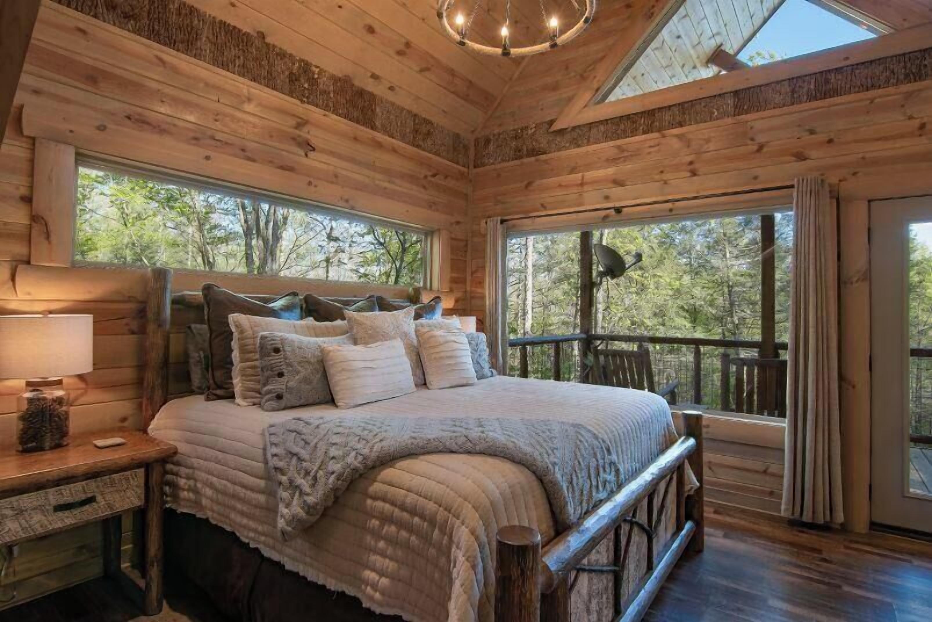 A cozy wooden cabin bedroom with a large bed, a nightstand, and a window overlooking the forest.