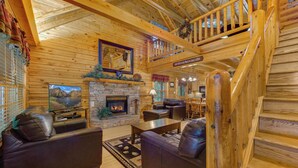 A cozy log cabin interior with a stone fireplace, leather sofas, and a dining area. - Leconte Lookout (Sevierville)