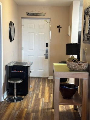 A hallway with a door, a small bar area with stools, a table with a basket, and a wall-mounted clock. - Mountain View Condo 3702 (Pigeon Forge)