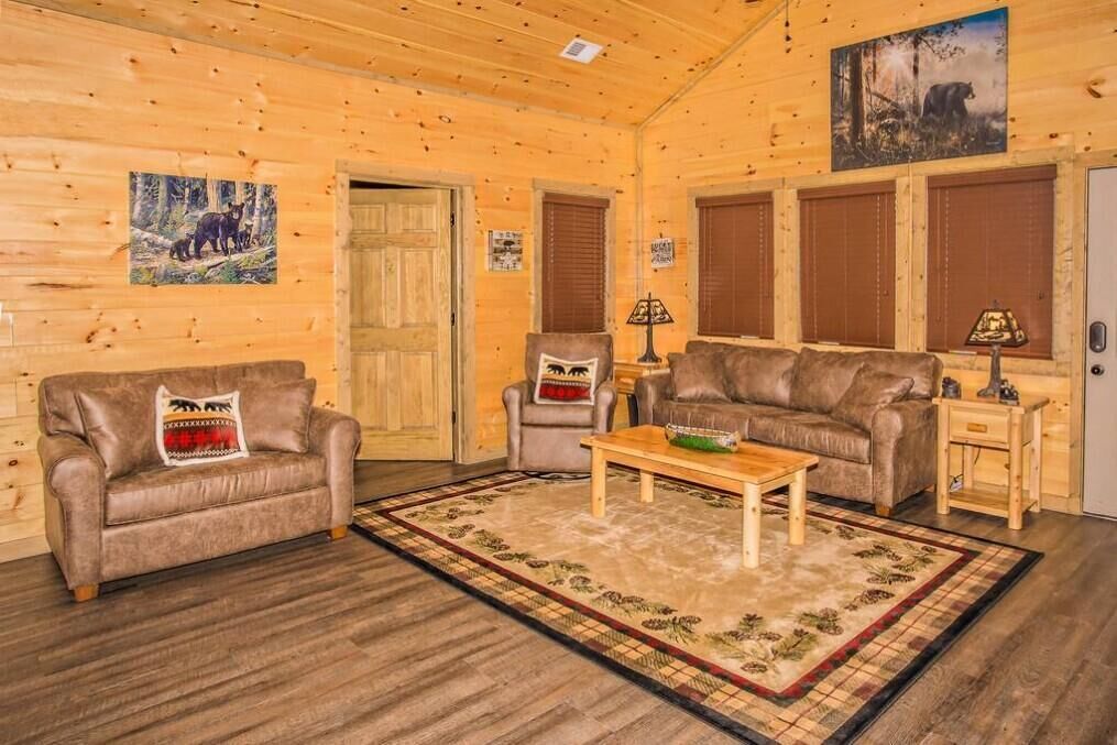 A log cabin interior with a wooden floor, two leather sofas, a coffee table, and a rug.