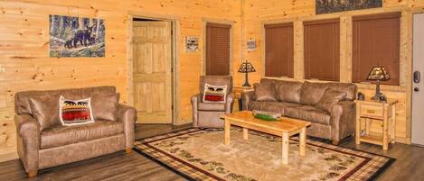 A log cabin interior with a wooden floor, two leather sofas, a coffee table, and a rug.