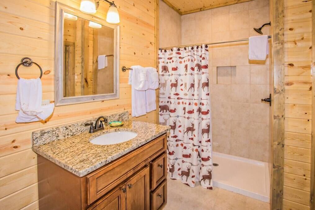 A wooden cabin bathroom with a granite countertop sink, a mirror, and a shower with a deer-patterned curtain.